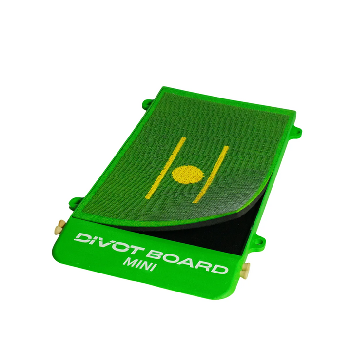 Divot Board MINI at an angle with the green turf pad peeled up off the black foam base, wooden tees in the edge