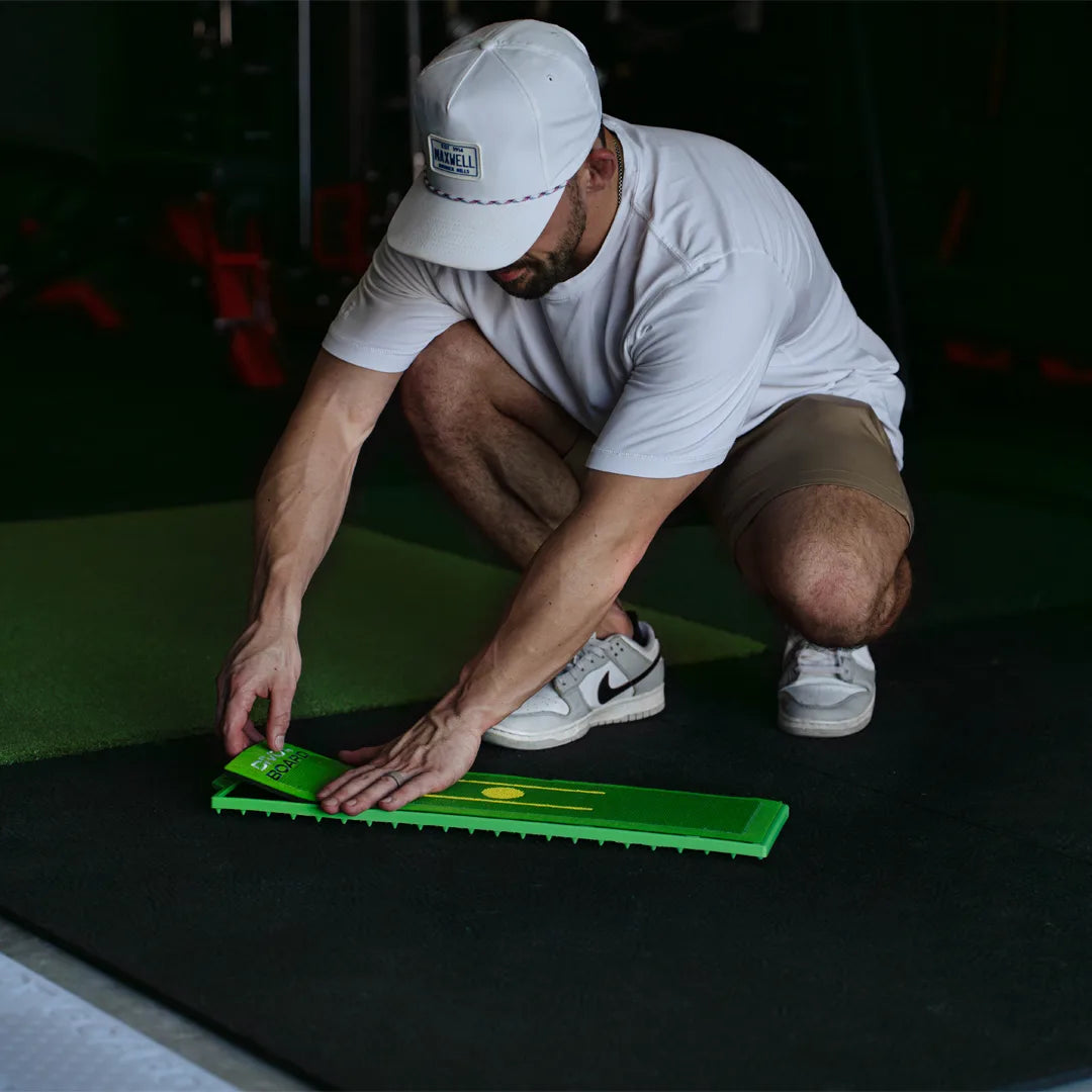 Man in a white cap pressing a fresh Divot Board replacement pad onto the board frame in an indoor hitting bay