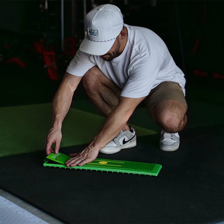 Man in a white cap pressing a fresh Divot Board replacement pad onto the board frame in an indoor hitting bay